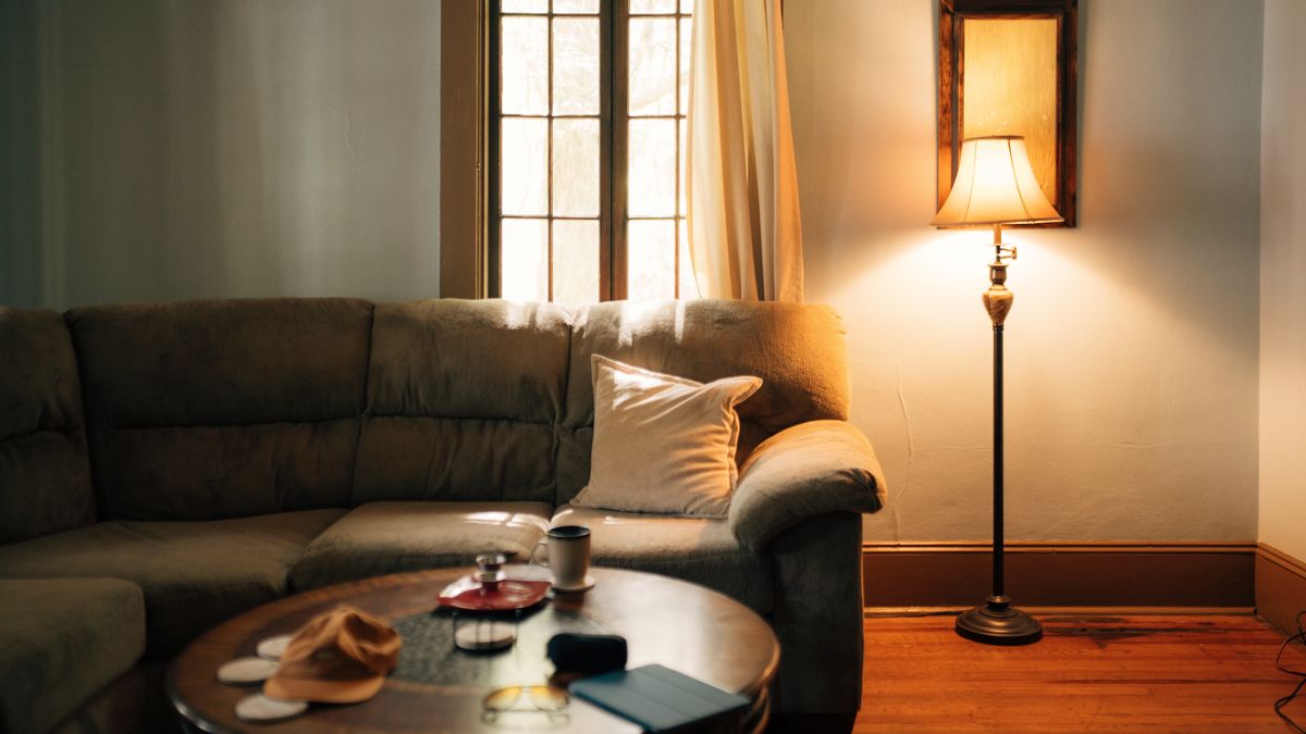 A living room at night, lit by a single floor lamp beside the sofa